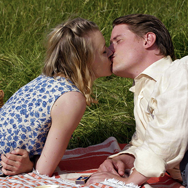 En man och en kvinna kysser varandra på en filt utomhus i soligt vårväder.