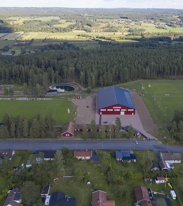 Ett flygfoto som visar den röda Furulidshallen med omgivande natur och bebyggelse. 
