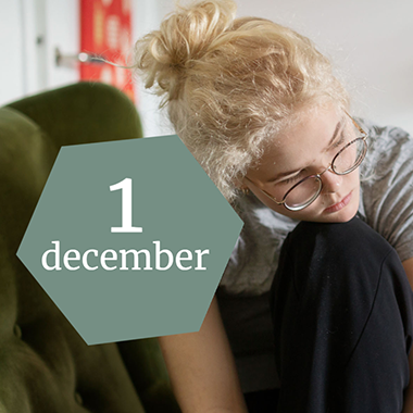 En ung tjej med blont hår och glasögon vilar hakan på sitt knä. Ovanpå fotot finns en grön hexagon med texten "1 december".