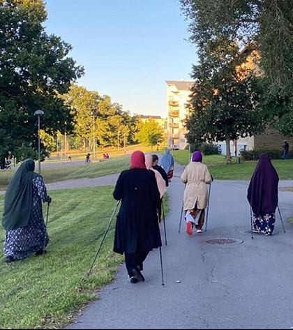 Flera kvinnor, klädda i slöja, promenerar med gåstavar utomhus.