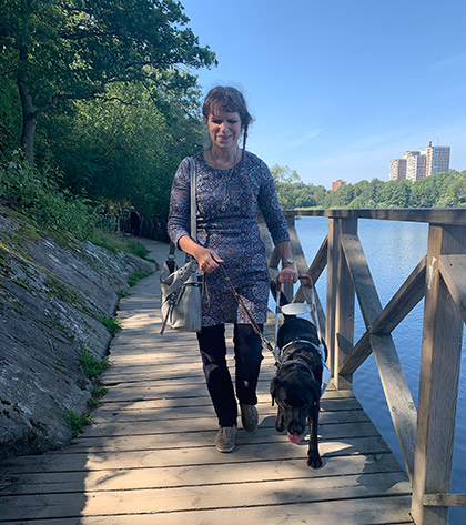 Projektledare för Lika Unika Akademi Tiina Nummi-Södergren ses promenerande på en trägång längs vattnet med en ledarhund.