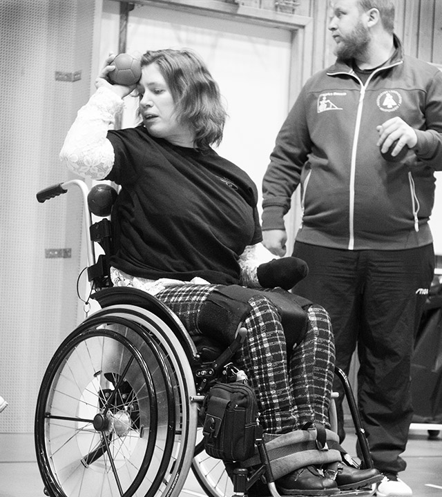 En kvinna i rullstol håller i en bocciaboll som hon håller upp mot ansiktet