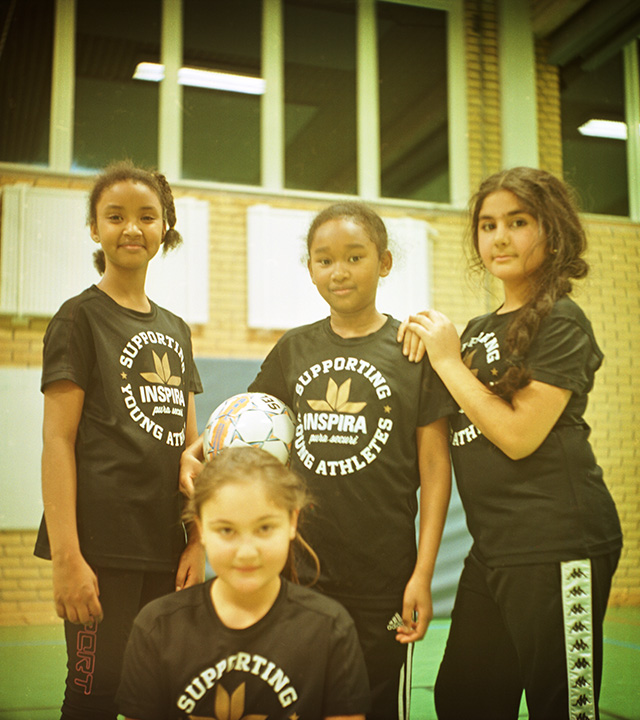 Fyra unga tjejer i träningskläder och en av tjejerna håller i en fotboll