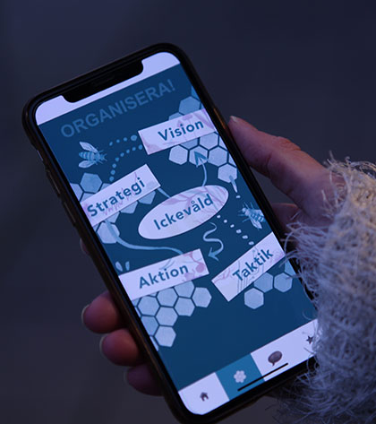 En hand håller i en mobiltelefon, på skärmen syns textrutor med texterna "Organisera", "Vision", "Strategi", "Ickevåld", "Aktion", "Taktik"